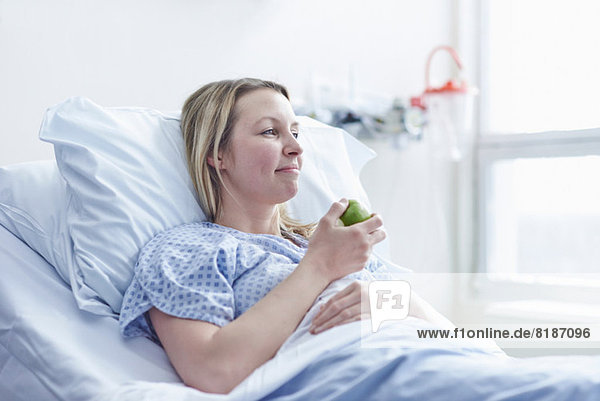 Patient liegt im Krankenhausbett und isst Apfel.