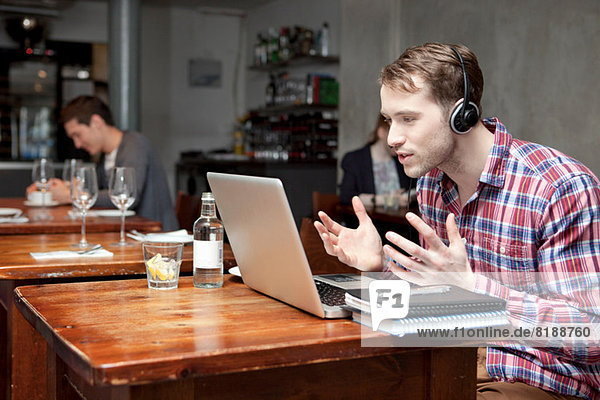 Young man wearing headphones using laptop in cafe