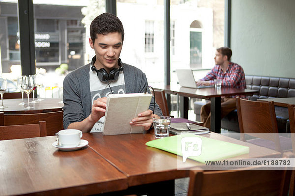 Junger Mann mit digitalem Tablett im Café