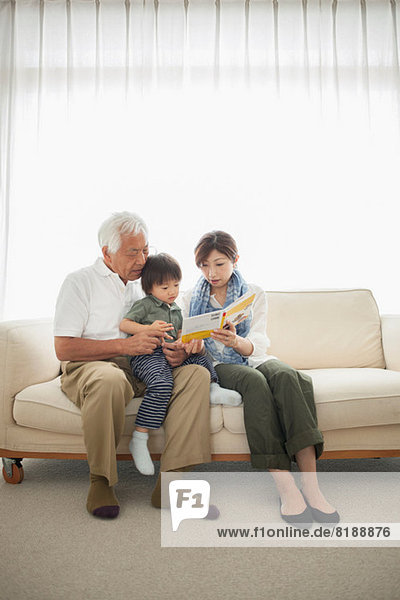 Mother reading to son sitting on grandfather's lap