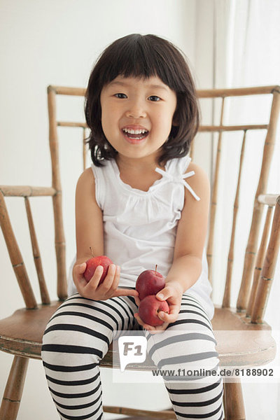 Girl sitting on wooden chair holding apples  portrait