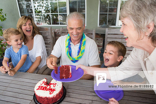 Seniorin serviert ein Stück Geburtstagskuchen auf der Party mit der Familie