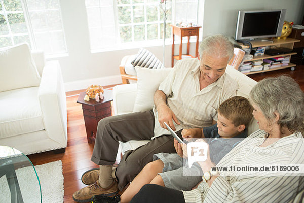 Großeltern sitzend mit Enkel und Blick auf digitales Tablett