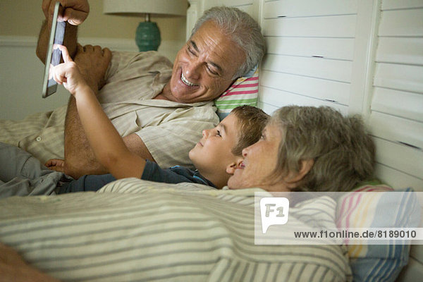 Großeltern liegend mit Enkel und Blick auf digitales Tablett