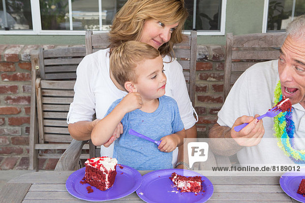 Enkel und Mutter sehen zu  wie der ältere Mann Geburtstagskuchen isst.
