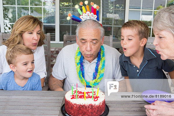 Senior Mann beim Ausblasen von Kerzen auf Geburtstagskuchen mit Familie