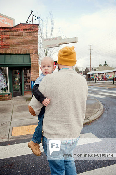 Vater trägt jungen Sohn über den Fußgängerüberweg
