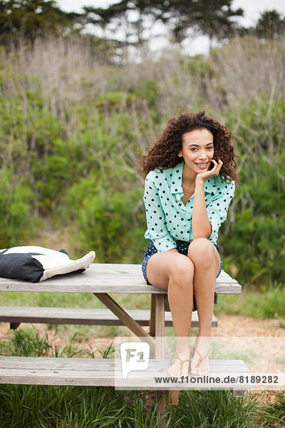 Junge Frau auf Picknicktisch sitzend lächelnd  Portrait