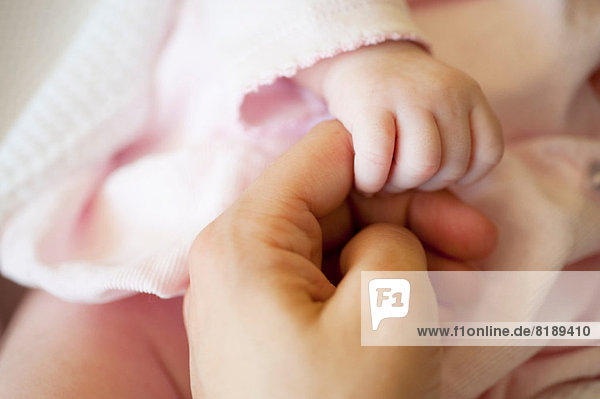 Baby girl holding mid adult woman's finger  close up