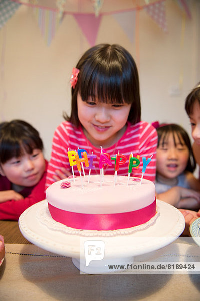 Mädchen schaut auf Geburtstagskerzen auf Kuchen