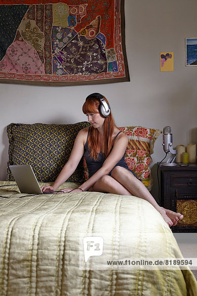 Mittlere erwachsene Frau auf dem Bett sitzend mit Laptop