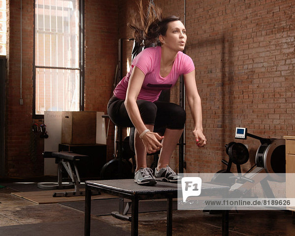 Junge Frau beim Springen auf dem Tisch im Fitnessstudio