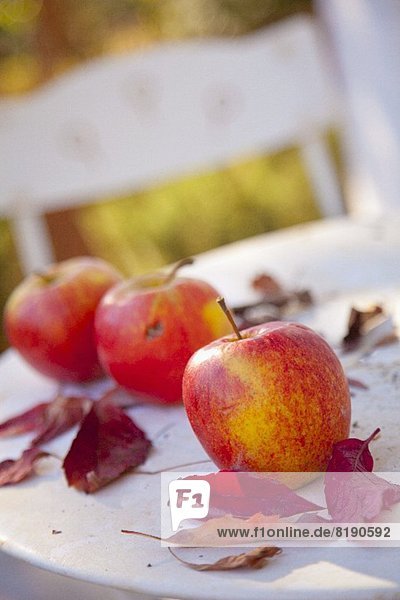 Drei Äpfel und rote Blätter auf einem Tisch