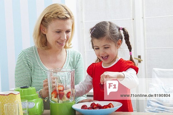 A mother and daughter preparing a strawberry milkshake