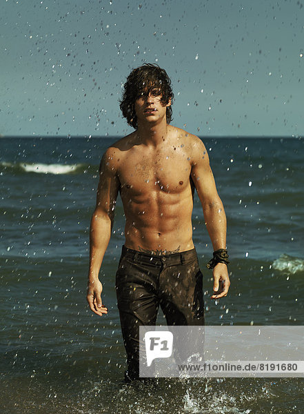 Mann mit nackter Brust und langer Hose im Meer stehend