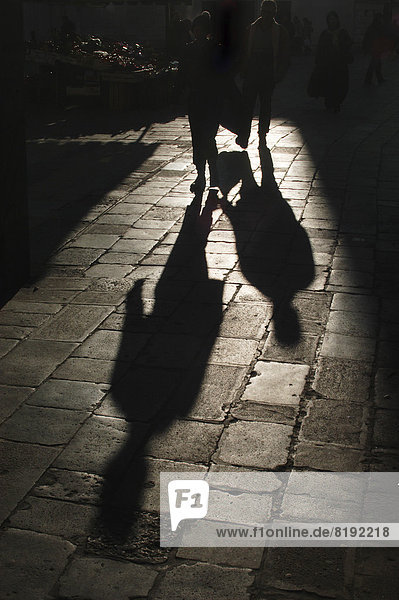 Pedestrians casting long shadows on the historic sidewalk