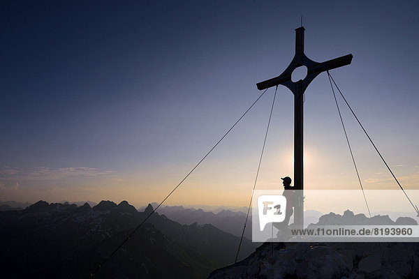 Mountaineer at the summit cross on Großer Krottenkopf Mountain at dusk