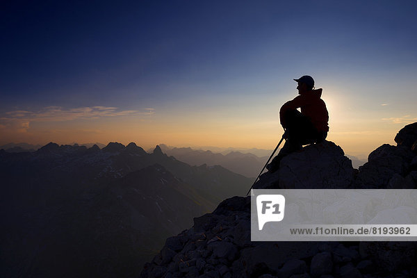 Bergsteiger sitzt auf einem Felsen auf dem Großen Krottenkopf  Abenddämmerung