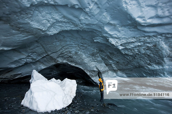 Mountaineer looking up at the ceiling of an ice cave  glacial stream flowing through an ice cave of Matanuska Glacier