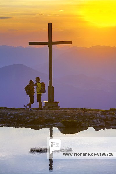 Paar bei Sonnenuntergang beim Gipfelkreuz in der Osterhorngruppe Salzburger Land Österreich