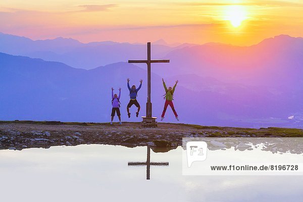 Jubelnde junge Leute bei Sonnenuntergang beim Gipfelkreuz in der Osterhorngruppe Salzburger Land Österreich