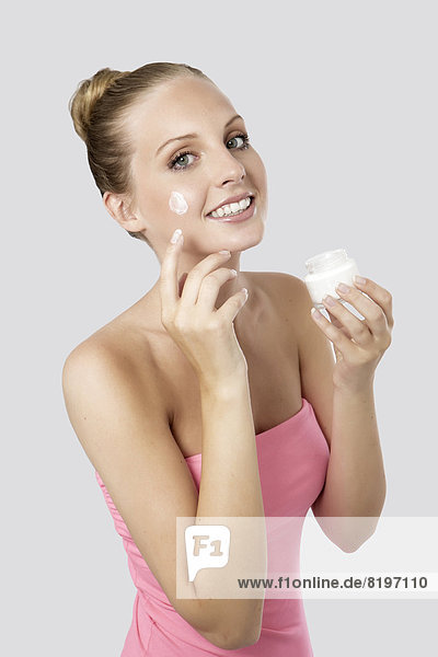 Portrait of young woman applying cream on face  smiling
