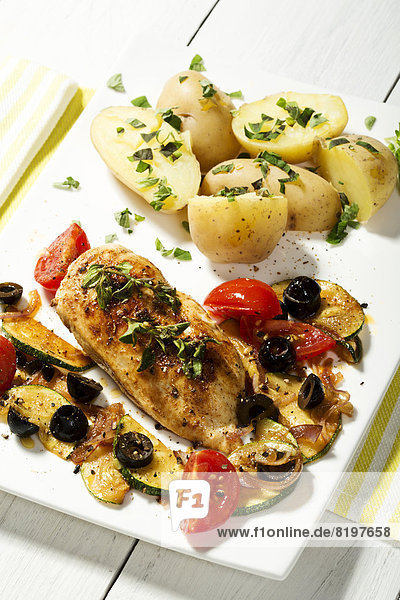 Plate of roasted chicken with potatoes  olives  tomatoes and garnished with herbs on wooden table  close up