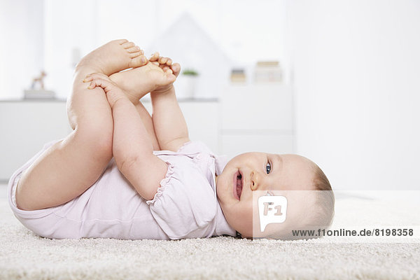 Germany,  North Rhine Westphalia,  ,  Baby girl lying on carpet,  smiling