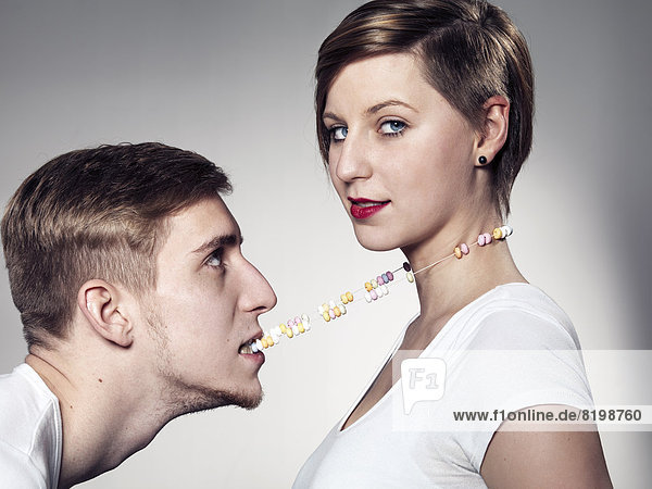 Junger Mann beißt Süßigkeiten Halskette  während die Frau in die Kamera sieht  Mund