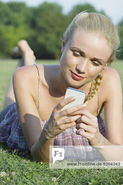 Frau auf Rasen liegend  mit Smartphone