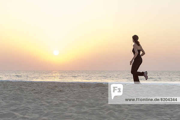 Frau beim Joggen am Strand bei Sonnenaufgang