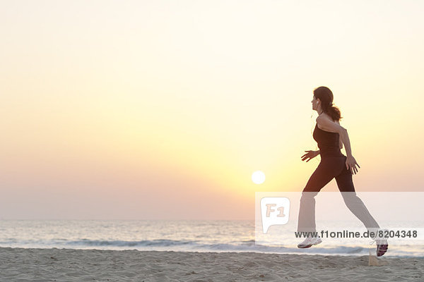 Frau beim Joggen am Strand bei Sonnenaufgang mit Kopfhörer