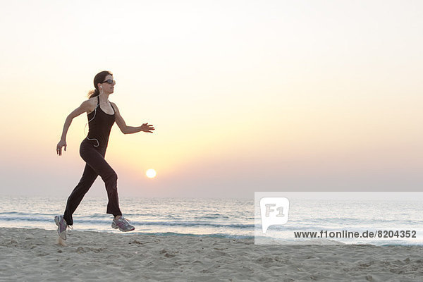 Woman with sunglasses jogging on beach at sunrise