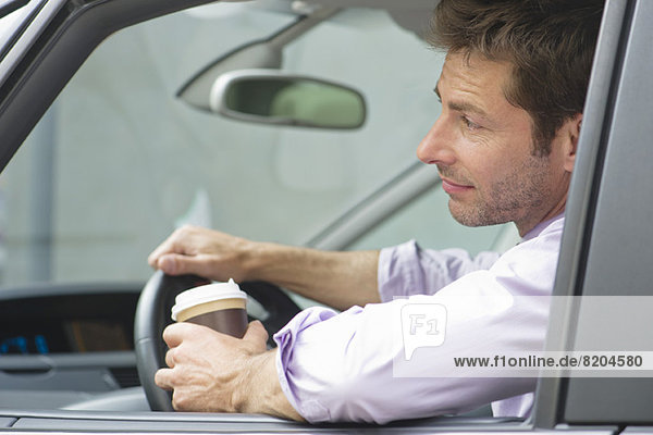 Mann fährt Auto mit Tasse Kaffee in einer Hand