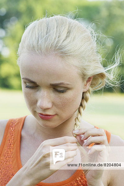 Young woman braiding hair  looking down in thought