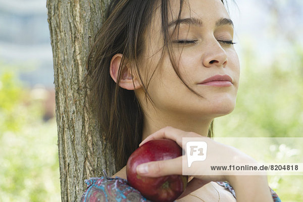Frau entspannt sich im Freien mit geschlossenen Augen und hält den Apfel.