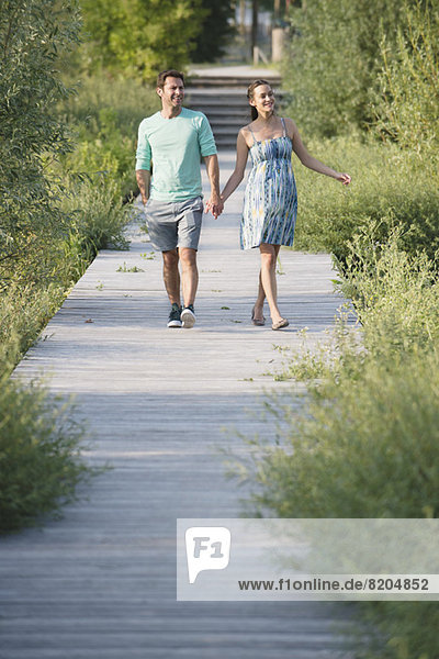 Couple holding hands enjoying walk along boardwalk through nature preserve
