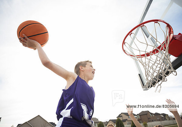 Caucasian boy dunking basketball in hoop