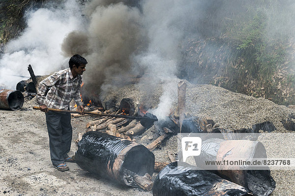 Ein Arbeiter vermischt Kies mit heißem Teer am offenem Feuer auf einer Straßenbaustelle