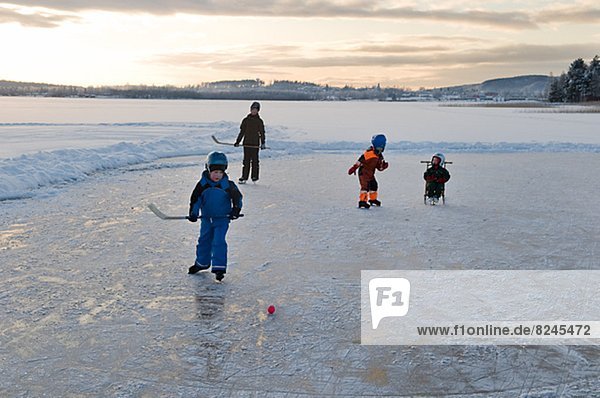 Children playing ice hockey on frozen lake