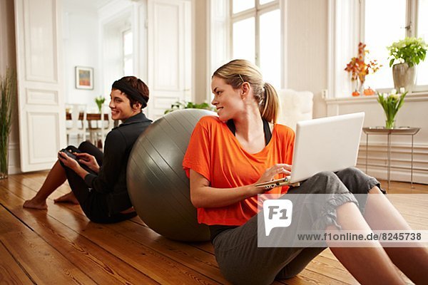 Two women sitting on floor leaning on fitness ball