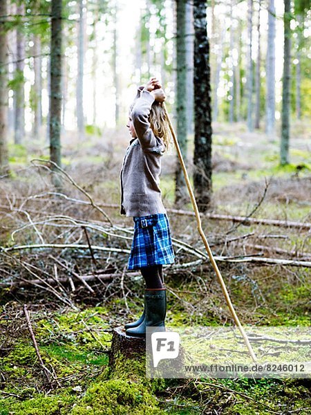 Girl standing on tree stump and holding stick