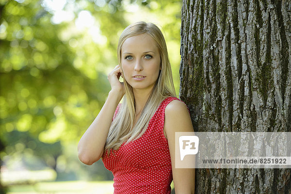 Young blond woman at a tree trunk in a park