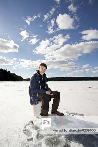 Porträt eines glücklichen jungen Mannes beim Eisfischen auf dem zugefrorenen See