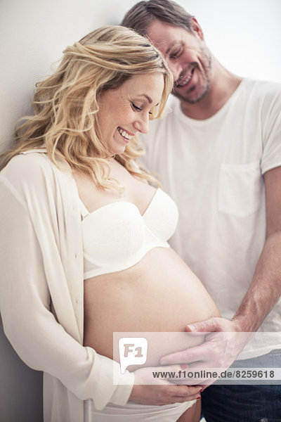 Glücklicher Mann  der zu Hause den Bauch einer schwangeren Frau berührt.