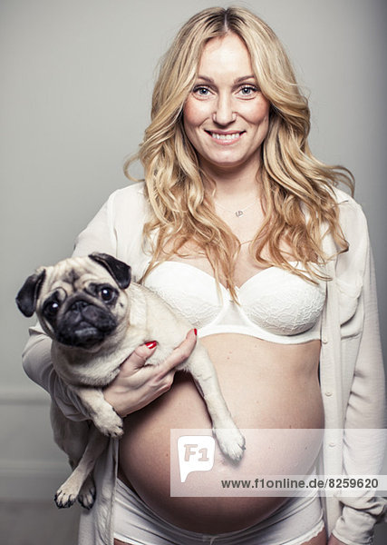 Portrait of happy pregnant woman holding pug dog at home