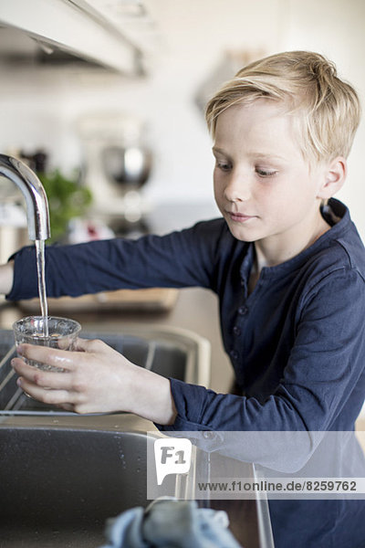 Junge füllt Wasser in Glas aus dem Wasserhahn in der Küche