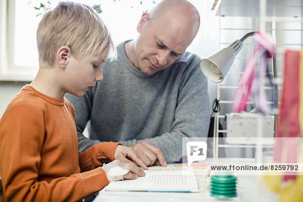 Vater hilft dem Sohn bei den Hausaufgaben am Tisch