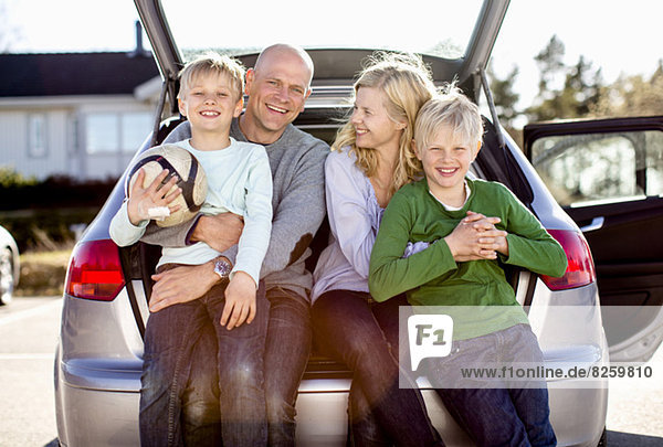 Porträt einer glücklichen Familie  die auf dem Kofferraum sitzt.