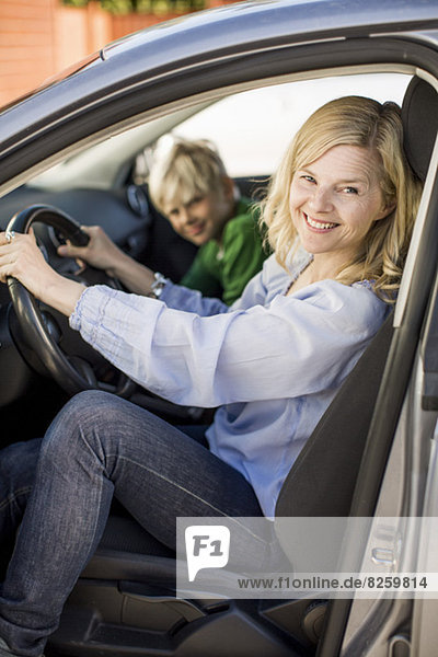 Portrait of happy woman driving car while sitting by son